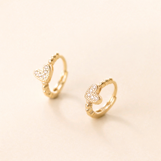 Gold hoop earrings with heart designs on a light beige background